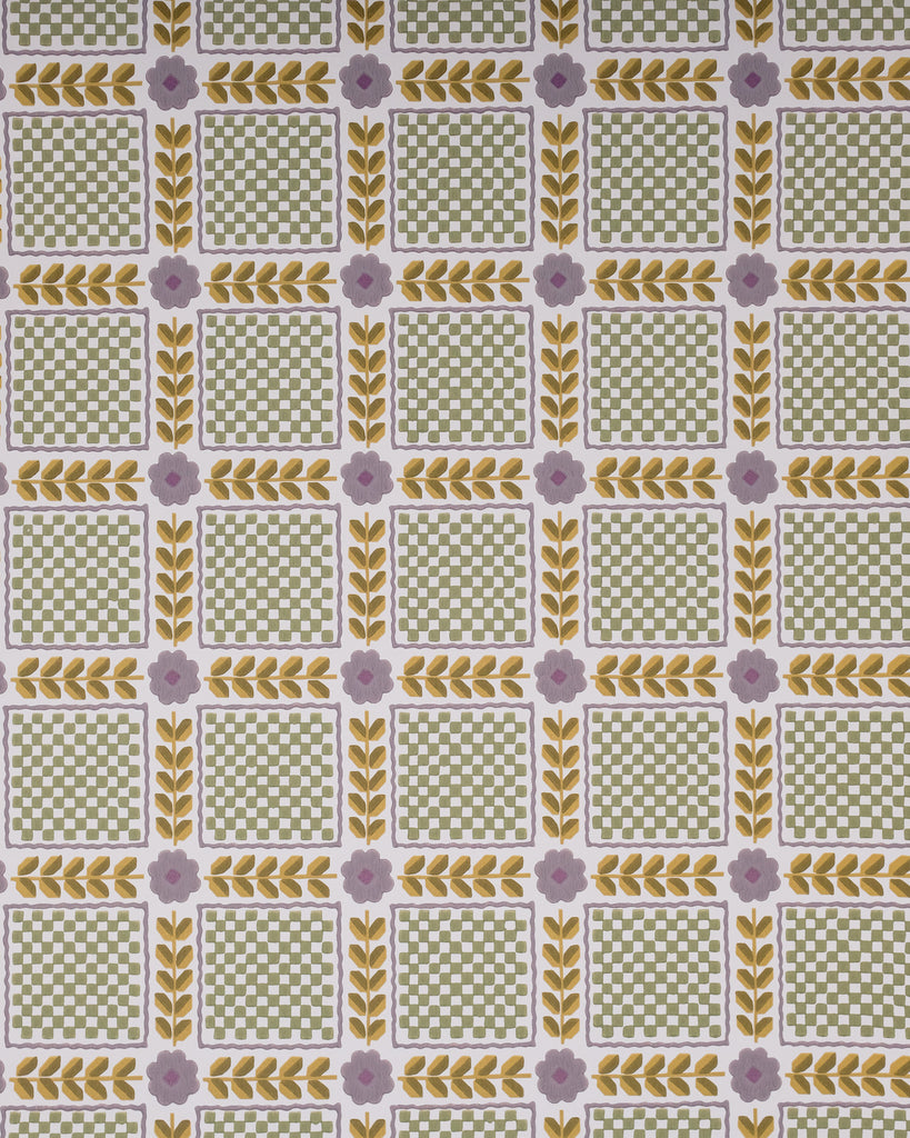 A close-up of a patterned fabric or wallpaper featuring a repeating grid of green and white checkered squares bordered by yellow leaf motifs and small lavender flowers, with pale pink flowers and green stems laid across the top.