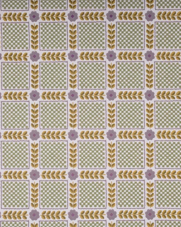 A close-up of a patterned fabric or wallpaper featuring a repeating grid of green and white checkered squares bordered by yellow leaf motifs and small lavender flowers, with pale pink flowers and green stems laid across the top.