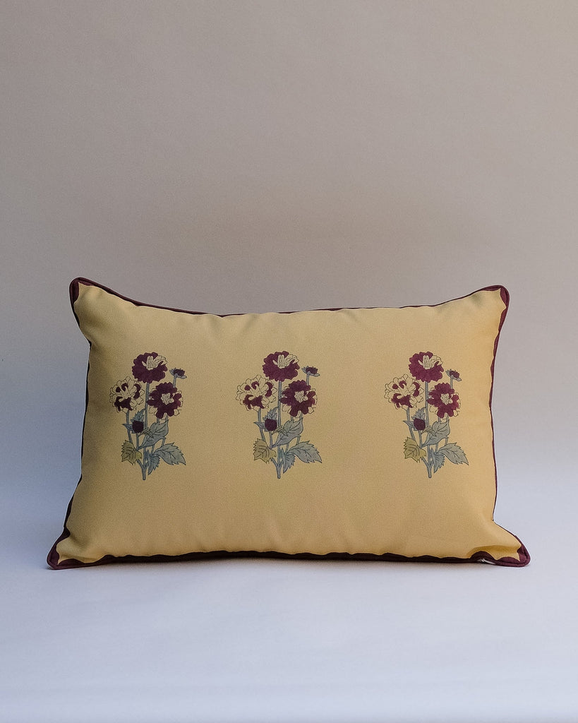 A decorative outdoor pillow with a retro floral pattern in muted shades of pink, purple, olive green, and beige, finished with dark brown piping.