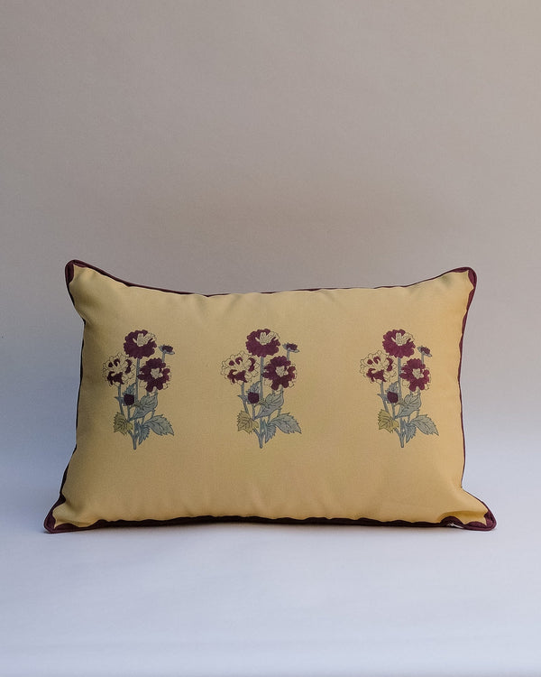 A decorative outdoor pillow with a retro floral pattern in muted shades of pink, purple, olive green, and beige, finished with dark brown piping.
