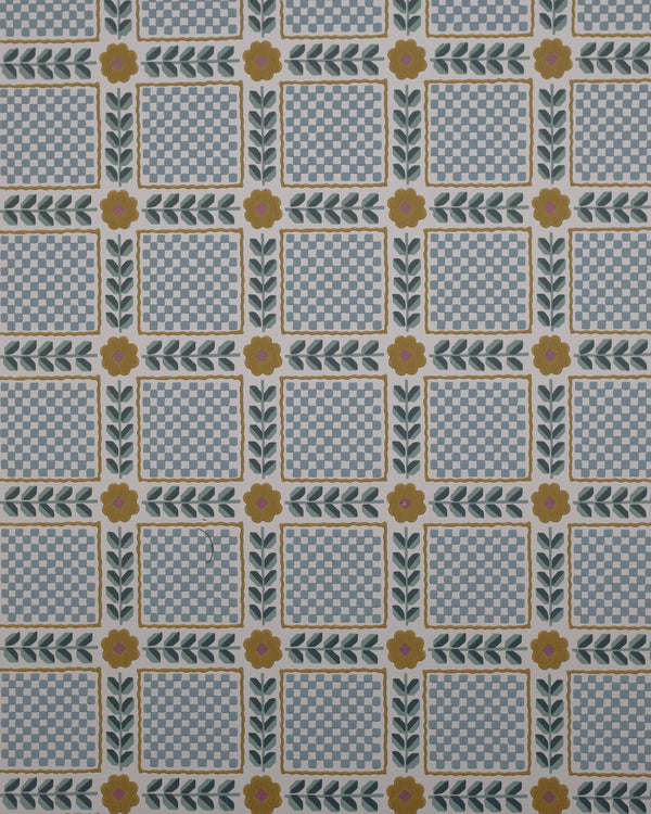 Mumtaz wallpaper finds beauty in order and repetition, with echoes of vintage patchwork and old hand-worked textiles. Tiny checks sit within leafy borders, punctuated by simple flowers, creating a rhythm that feels both nostalgic and playful. There is a quiet charm to its geometry—the kind of pattern that reveals more of itself the longer you live with it.