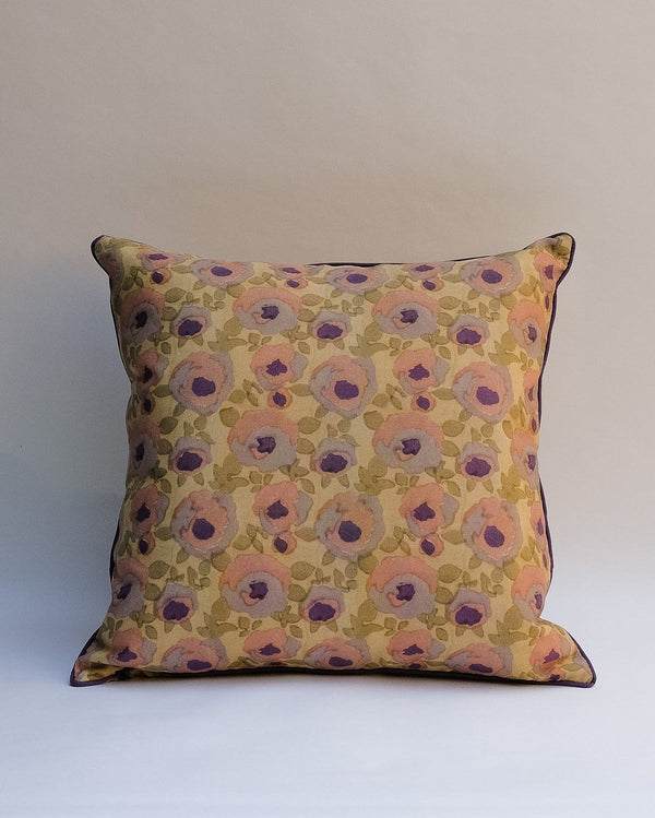 A square decorative outdoor pillow with a retro floral pattern in muted shades of pink, purple, olive green, and beige, finished with dark brown piping.