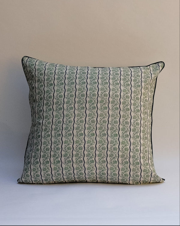 A square decorative throw pillow with a vertical wavy pattern in sage green and beige, finished with a thin black piped edge, set against a plain beige background.
