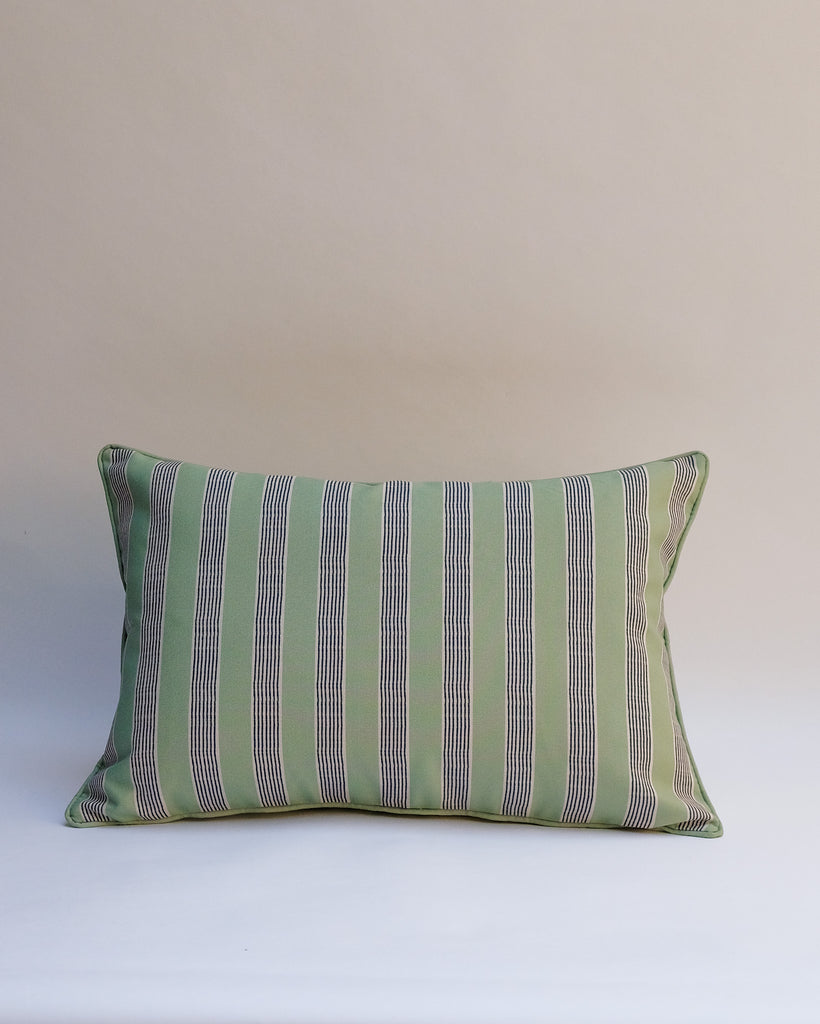 A rectangular throw pillow with vertical stripes in sage green, gray, and thin white lines, set against a plain beige background.