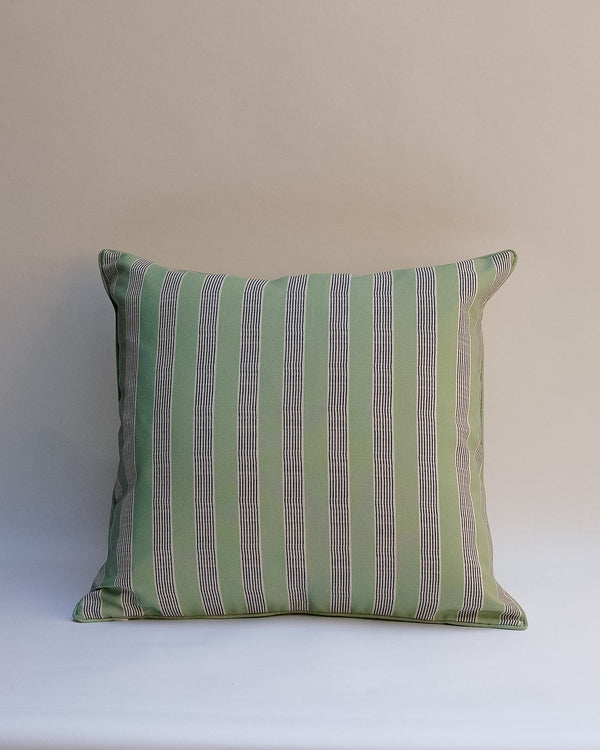 A square decorative throw pillow with vertical stripes in sage green, olive, and gray, resting on a white surface against a neutral beige background.