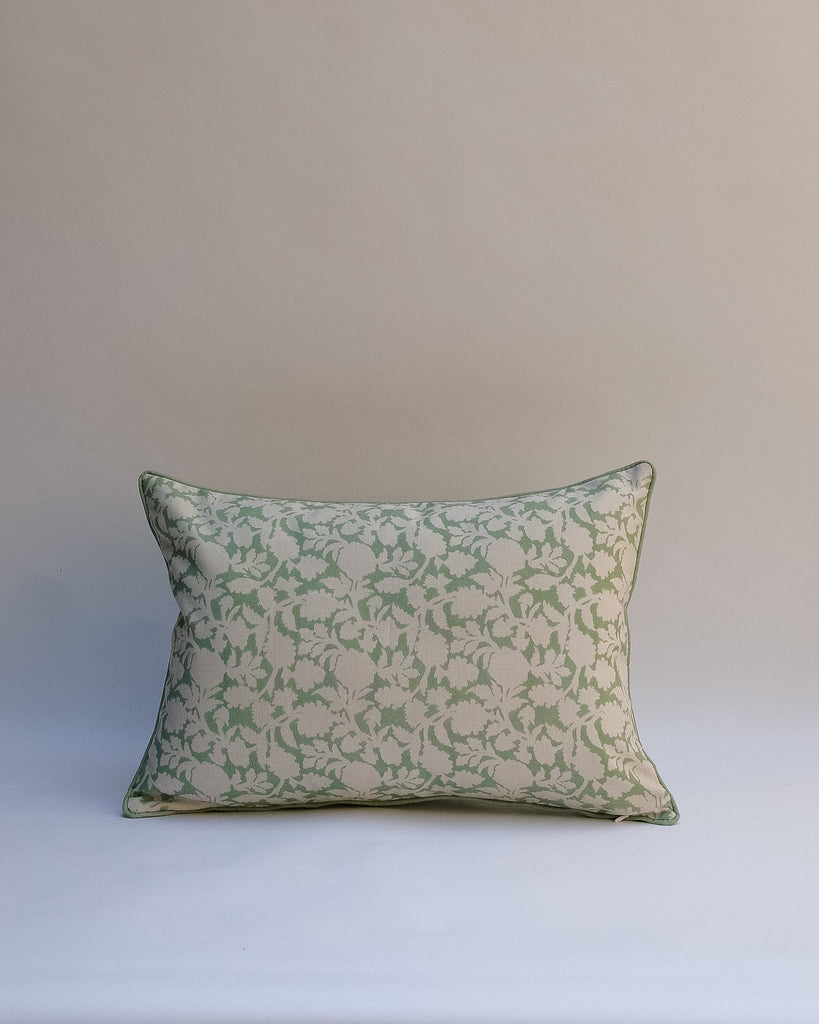 A rectangular decorative throw pillow with a sage green floral damask pattern on a cream background, set against a neutral beige studio backdrop.