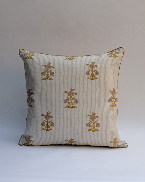 A square decorative outdoor pillow with a retro floral pattern in muted shades of pink, purple, olive green, and beige, finished with dark brown piping.