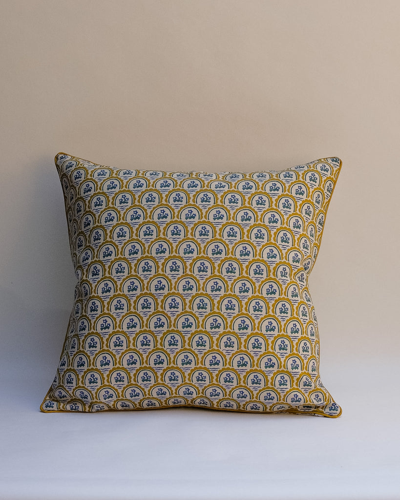A square decorative outdoor pillow with a retro floral pattern in muted shades of pink, purple, olive green, and beige, finished with dark brown piping.
